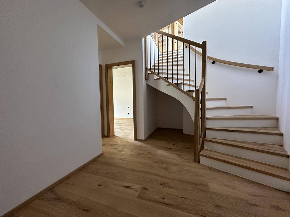 Heller Flur mit Holztreppe und Parkettboden, der die Etagen verbindet.