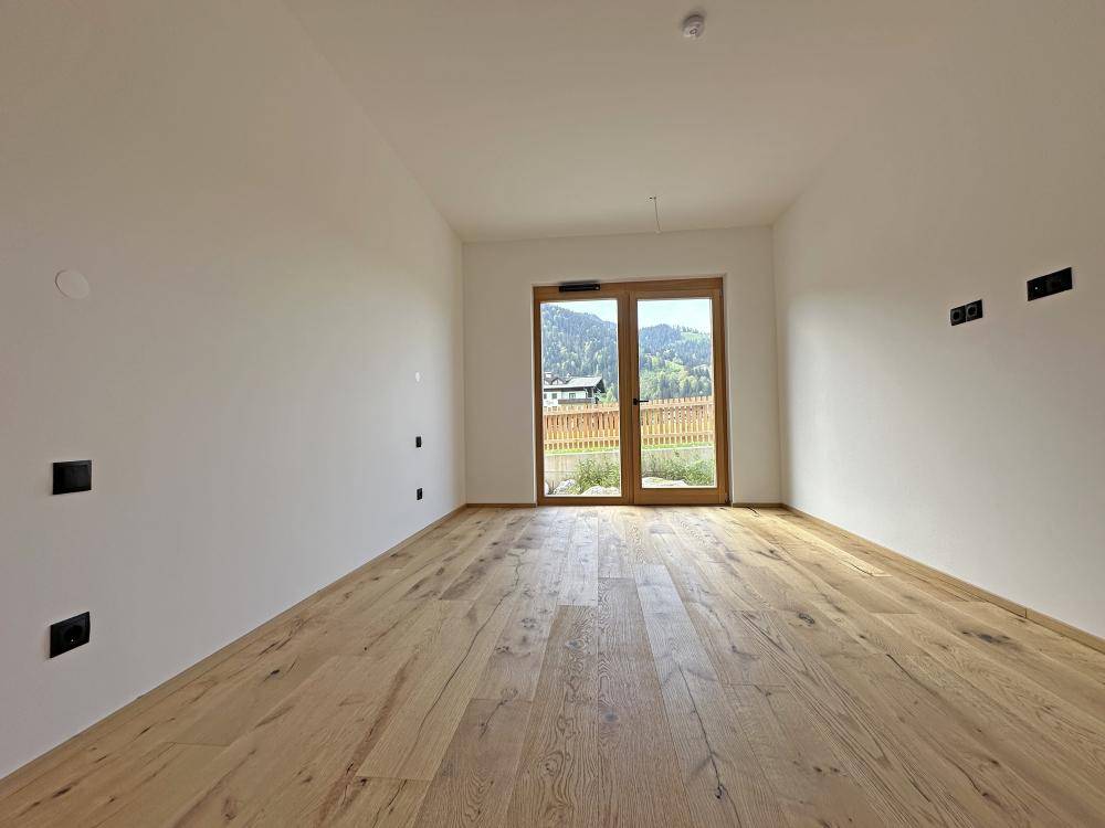 Heller Raum mit Holzboden und einer Tür, die zu einem Außenbereich führt.