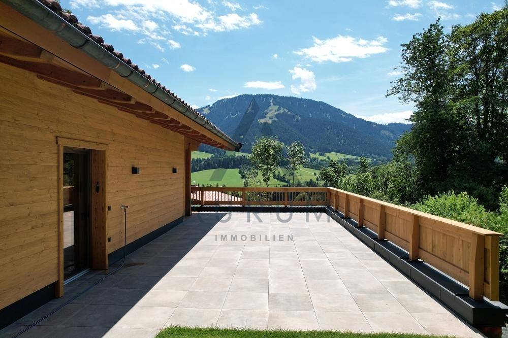Geräumige Terrasse mit Fliesenboden und Holzgeländer, bietet einen weiten Blick auf die umliegende Berglandschaft.