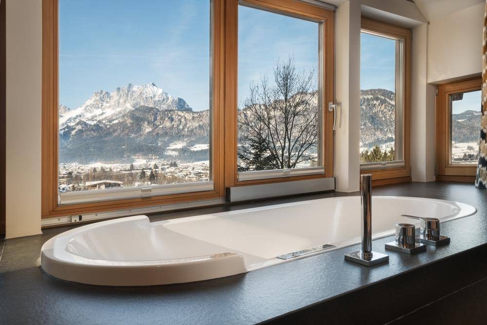 Modernes Badezimmer mit eingelassener Badewanne und großen Fenstern mit Bergblick.