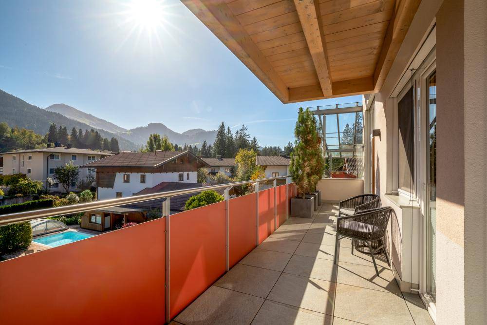 Sonniger Balkon mit Sitzgelegenheiten, Blick auf die Berge und einen Swimmingpool.