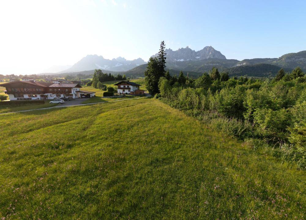 Idyllische Landschaft mit grünen Wiesen, traditionellen Häusern und beeindruckender Bergkulisse bei Sonnenlicht.