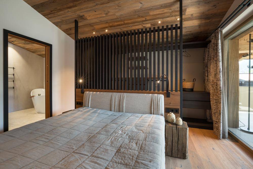Schlafzimmer mit Holzbalkendecke, Holzboden und Blick auf das angrenzende moderne Badezimmer.