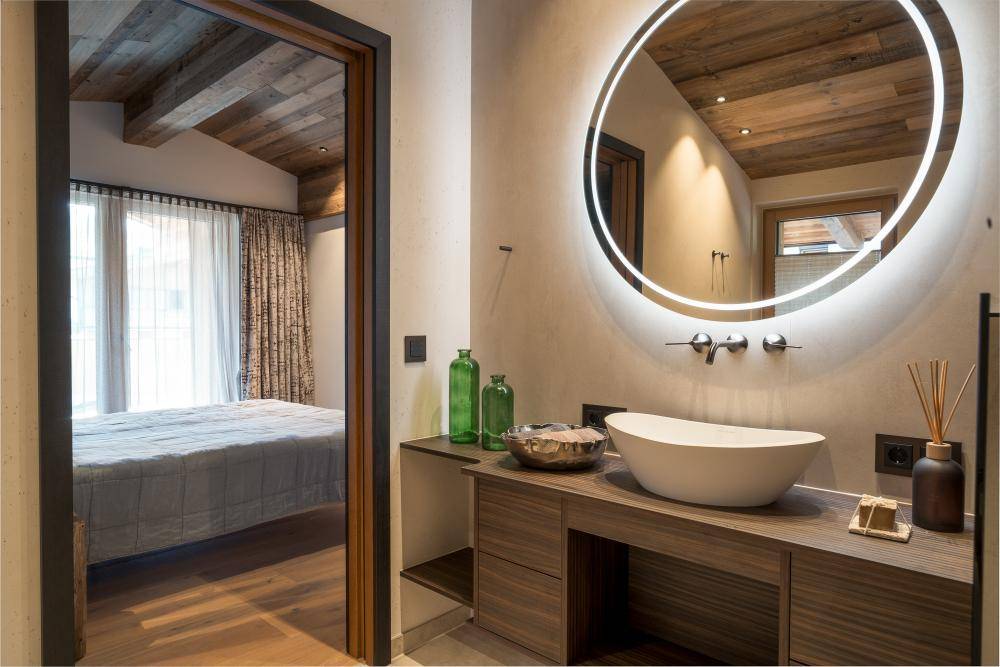 Elegantes Badezimmer mit Aufsatzwaschbecken, beleuchtetem Spiegel und Blick ins Schlafzimmer.