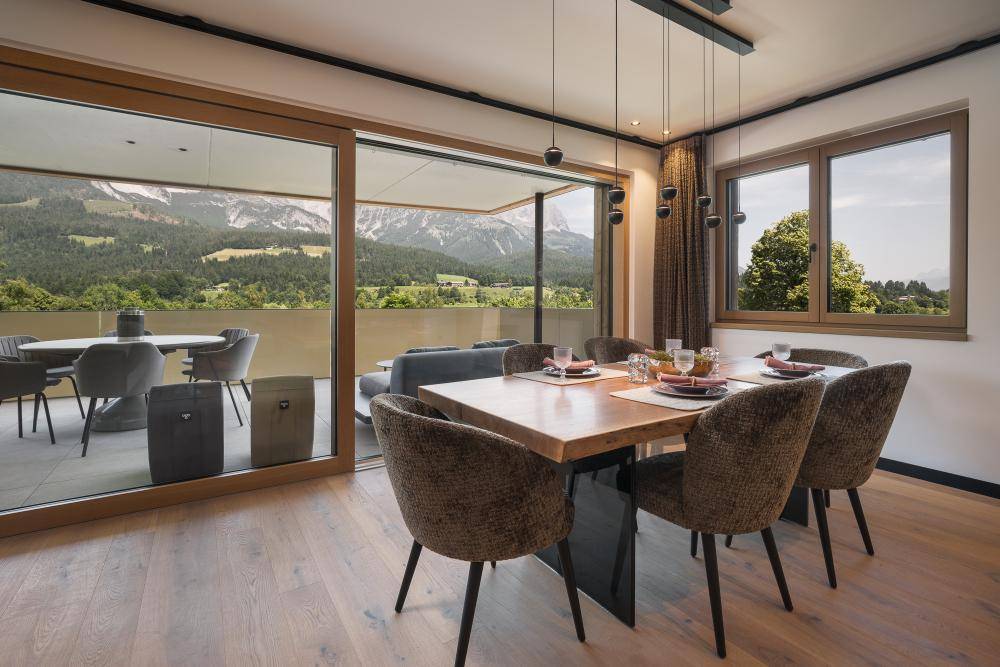 Heller Essbereich mit Holztisch und beeindruckendem Bergblick durch bodentiefe Fenster.