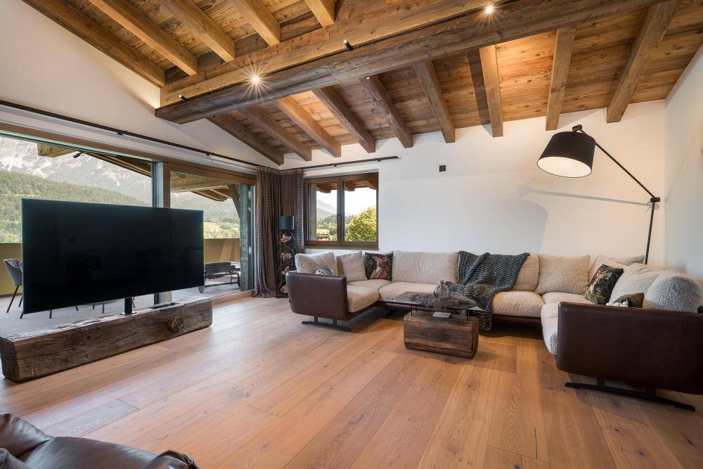 Helles Wohnzimmer mit großem Sofa, Holzbalkendecke und Panoramablick auf die Berge.