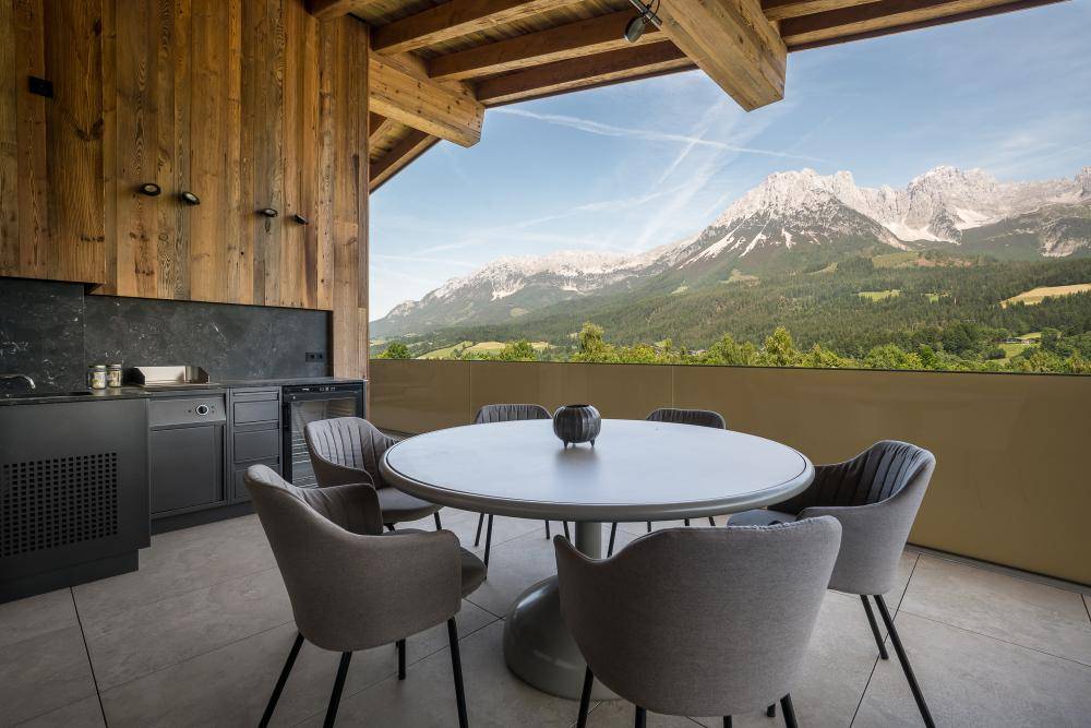 Moderne Außenküche auf einer Terrasse mit Esstisch und atemberaubendem Bergblick.