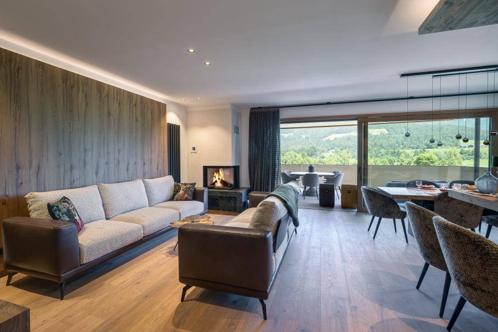 Heller Wohn-Essbereich mit Kamin, Holzboden und Panoramablick auf die Berge.