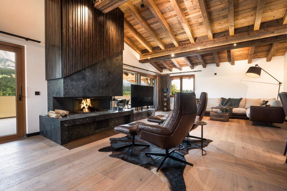 Großzügiges Wohnzimmer mit modernem Kamin, Holzbalkendecke und bequemen Ledersesseln.