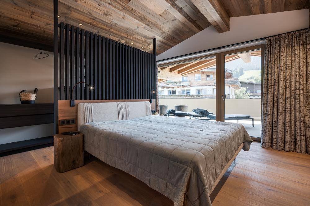 Gemütliches Schlafzimmer mit Holzbalkendecke, Doppelbett und Zugang zu einem Balkon.