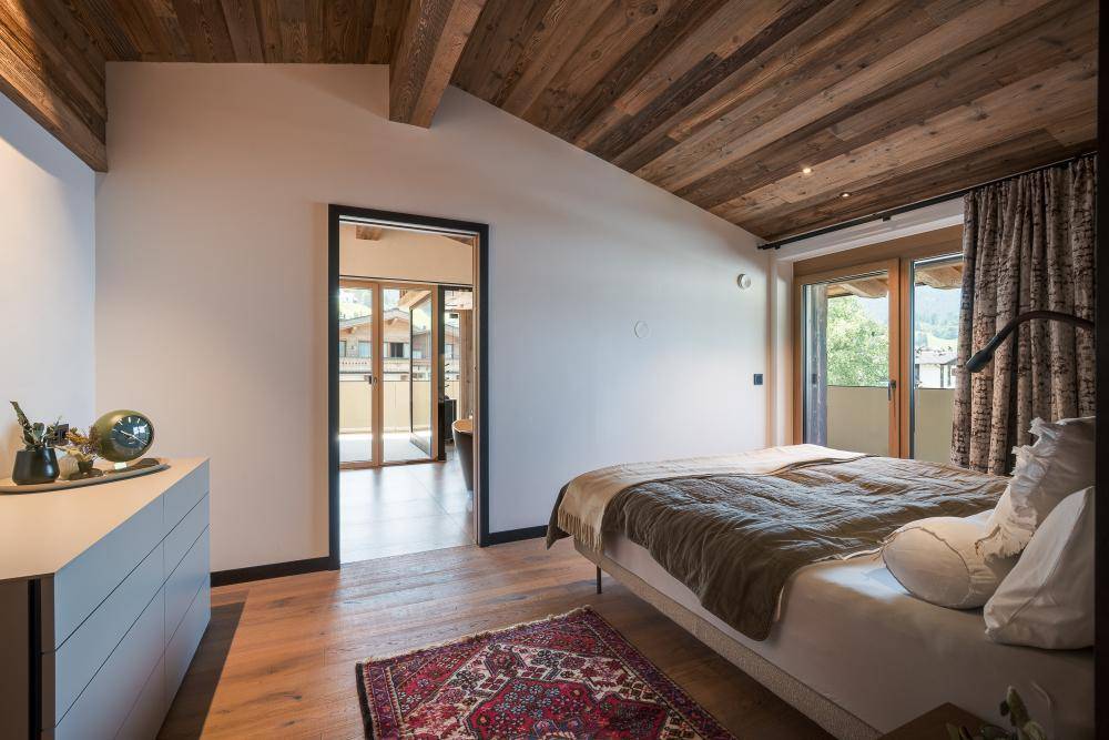 Helles Schlafzimmer mit Holzboden, Kommode und Zugang zu einem weiteren Raum oder Balkon.