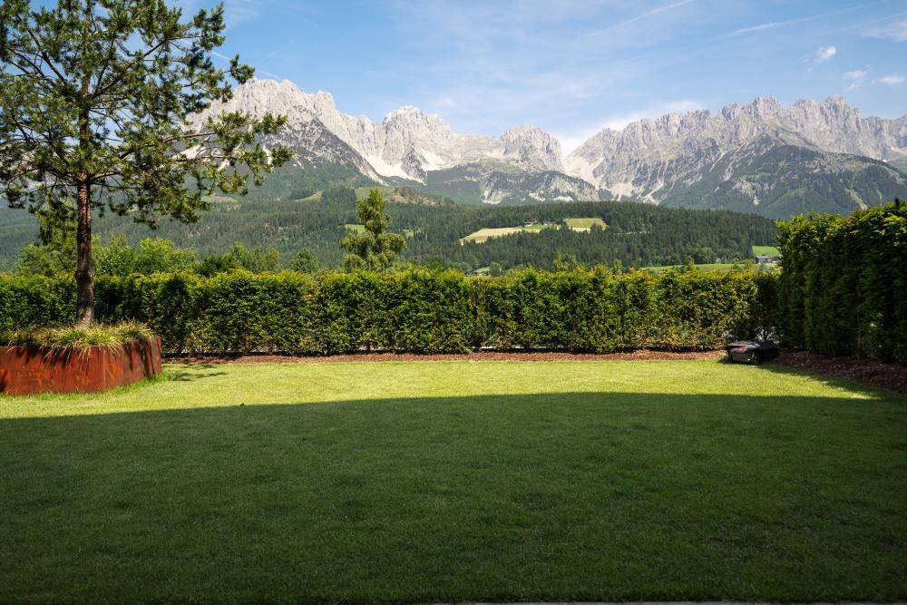 Gepflegter Garten mit Rasenfläche, Hecke und weitem Blick auf die Berge.