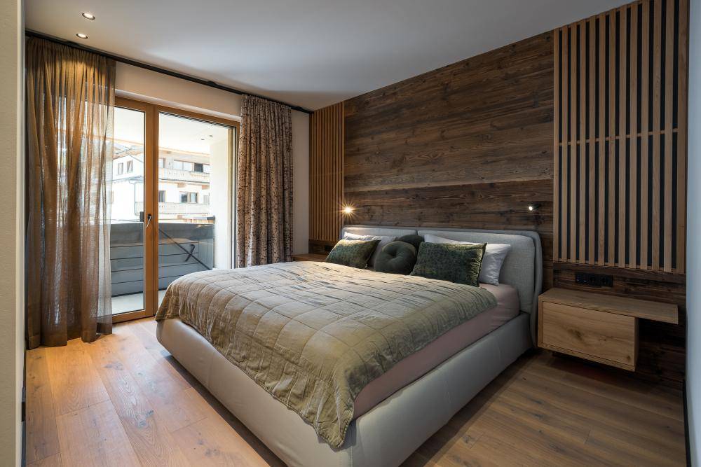 Gemütliches Schlafzimmer mit Holzwand, großem Bett und Zugang zum Balkon.