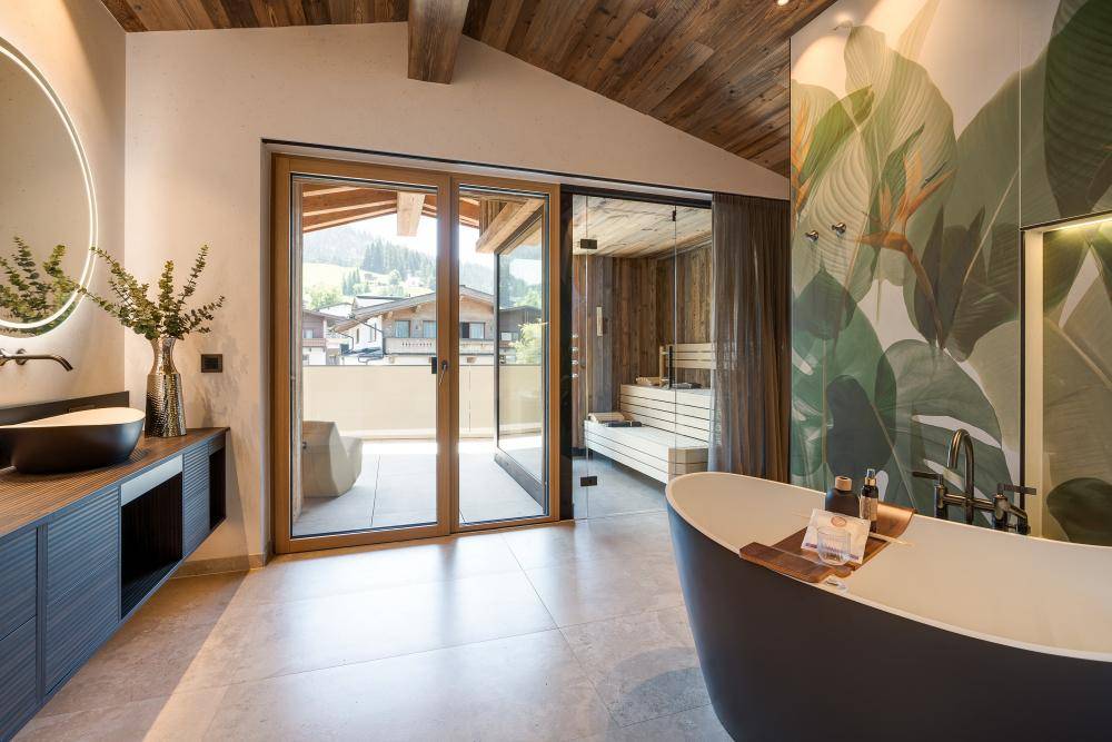 Luxuriöses Badezimmer mit freistehender Badewanne, Sauna und Zugang zu einem Balkon.