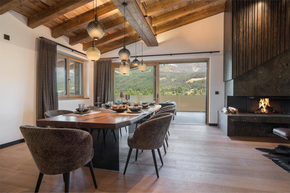 Gemütlicher Essbereich mit Holztisch, Kamin und Zugang zu einem Balkon mit Bergblick.