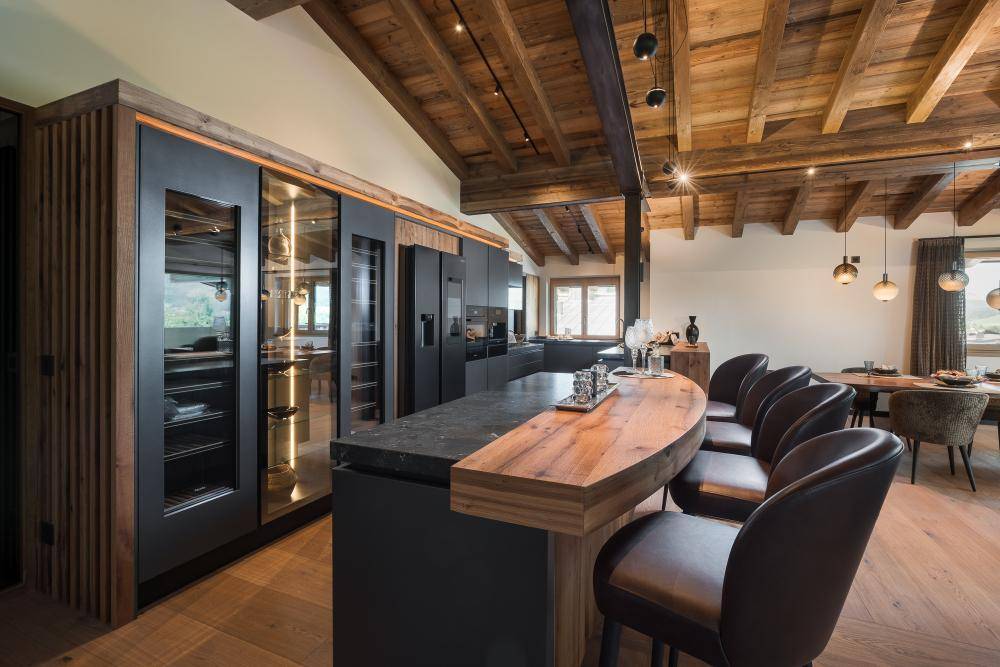 Moderne Küche mit Kücheninsel, Frühstücksbar und integrierten Weinkühlern unter Holzbalkendecke.