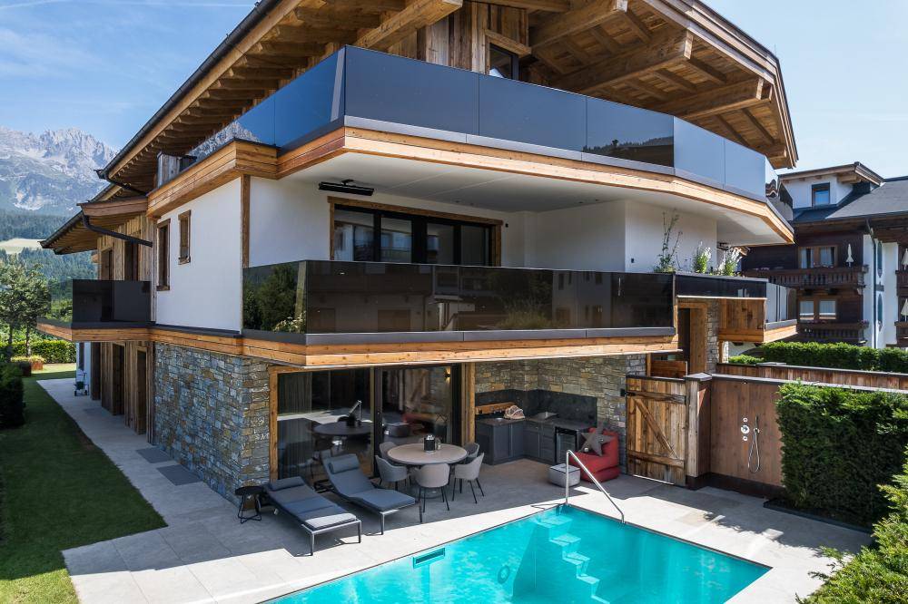 Luxuriöse Terrasse mit Pool, Liegestühlen und integrierter Außenküche am modernen Chalet.