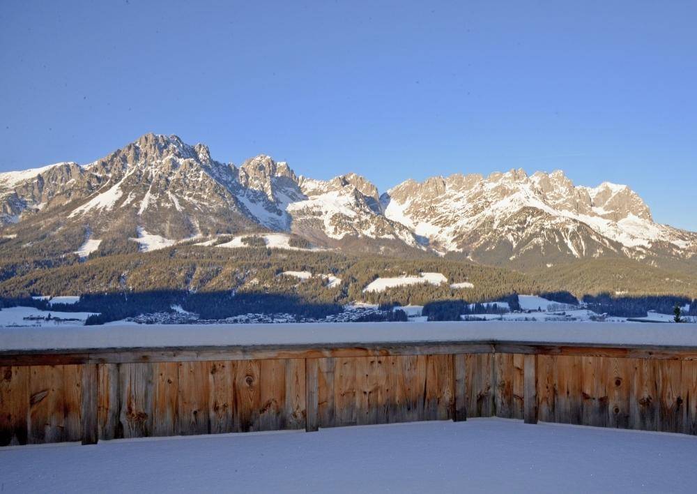 Balkon mit Holzgeländer und weitem Blick auf schneebedeckte Berge im Winter.