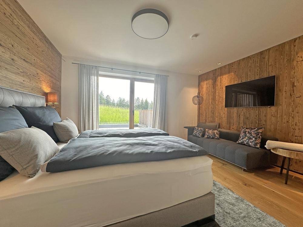 Schlafzimmer mit Holzwand, Doppelbett und Zugang zu einem Außenbereich.