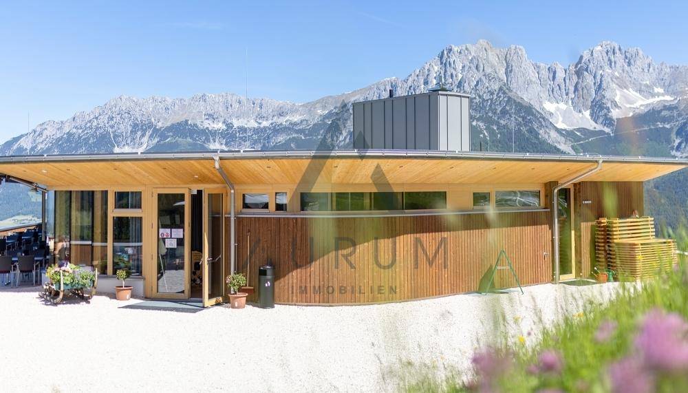 Nahaufnahme der modernen Holzfassade des Gebäudes mit großen Fenstern und majestätischer Bergkulisse.