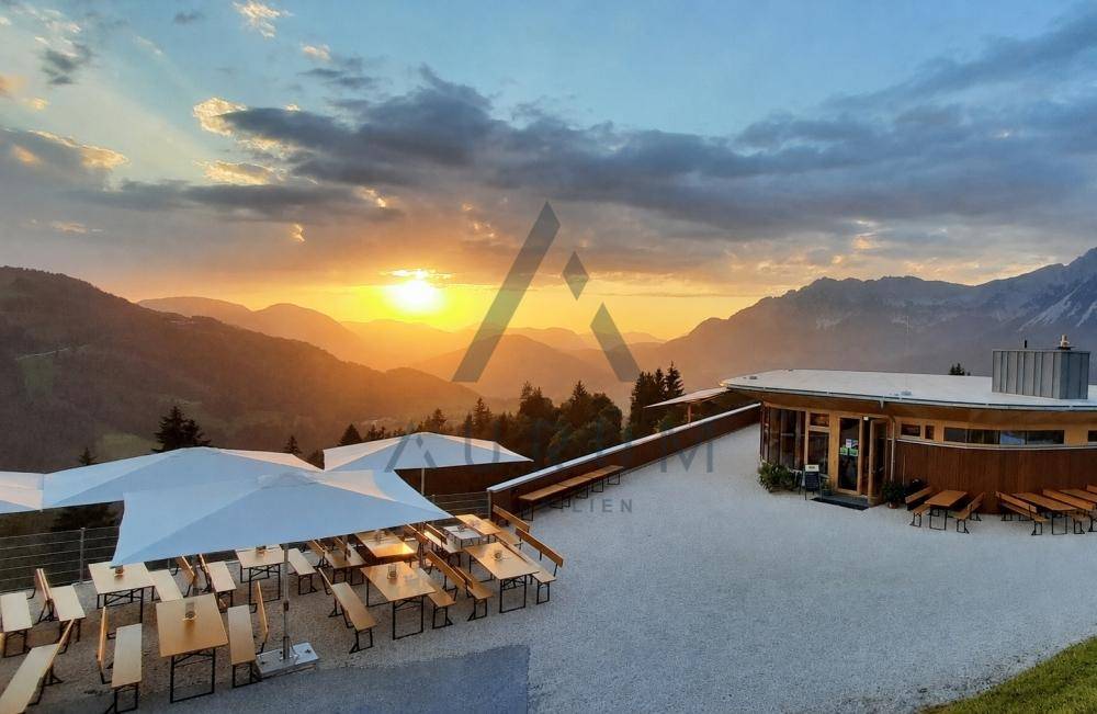 Große Terrasse mit Außensitzplätzen und Panoramablick auf einen atemberaubenden Sonnenuntergang über den Bergen.