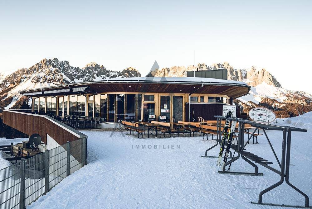 Das Gebäude im Winter, umgeben von Schnee, mit majestätischen Bergen im Hintergrund und Sitzbänken.