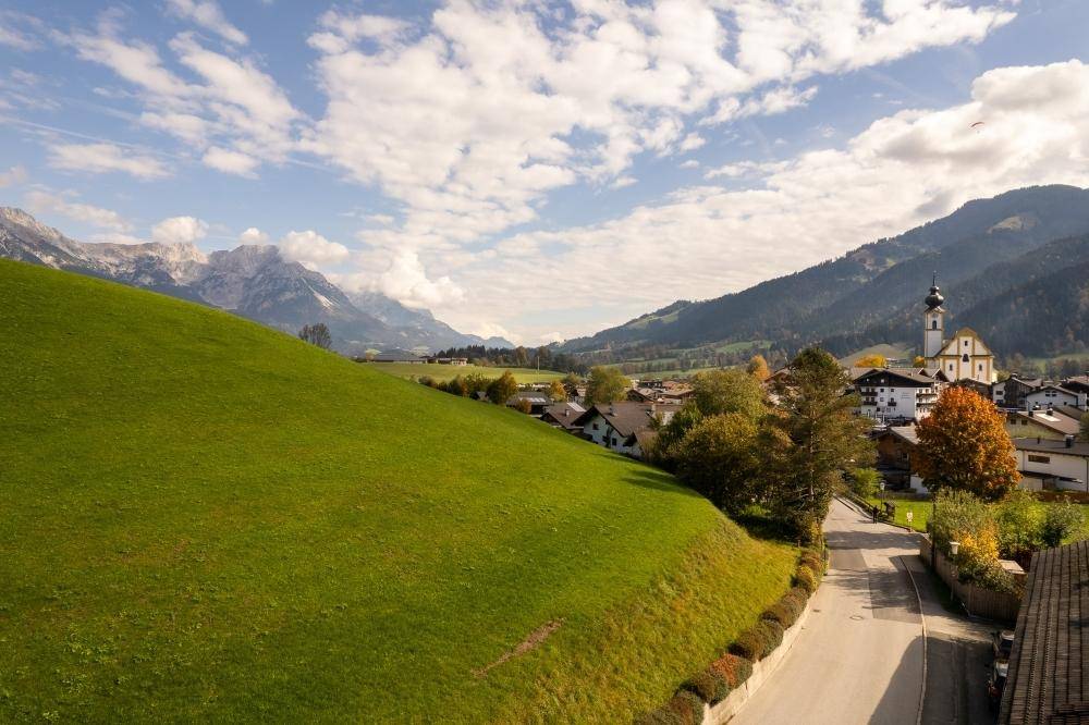 Malerische Alpenlandschaft mit Dorf, Kirche und Bergen unter blauem Himmel.