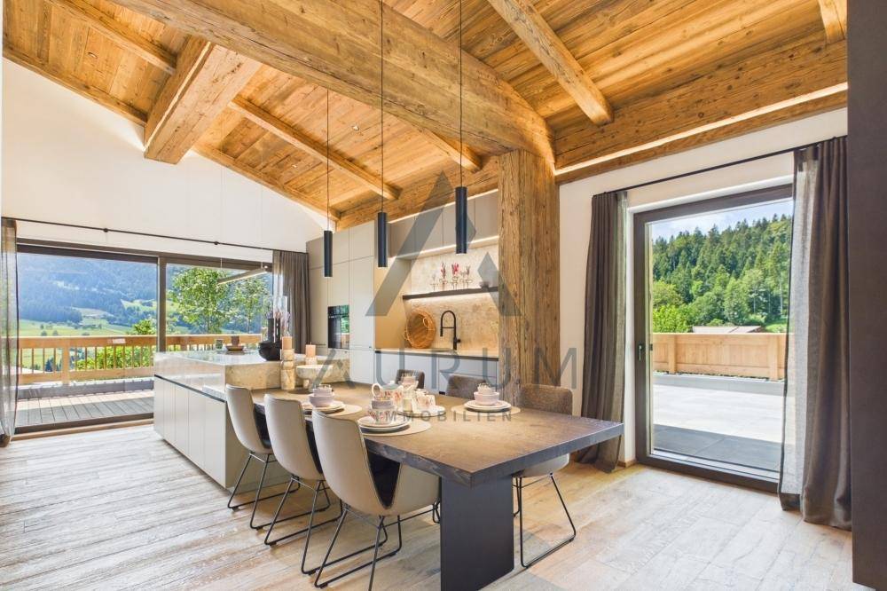 Offener Wohn-Essbereich mit moderner Küche, Holzbalkendecke und Bergblick.