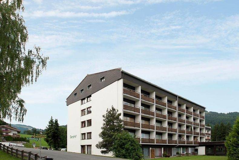 Mehrstöckiges Gebäude mit zahlreichen Balkonen, umgeben von Bäumen und grünen Hügeln.