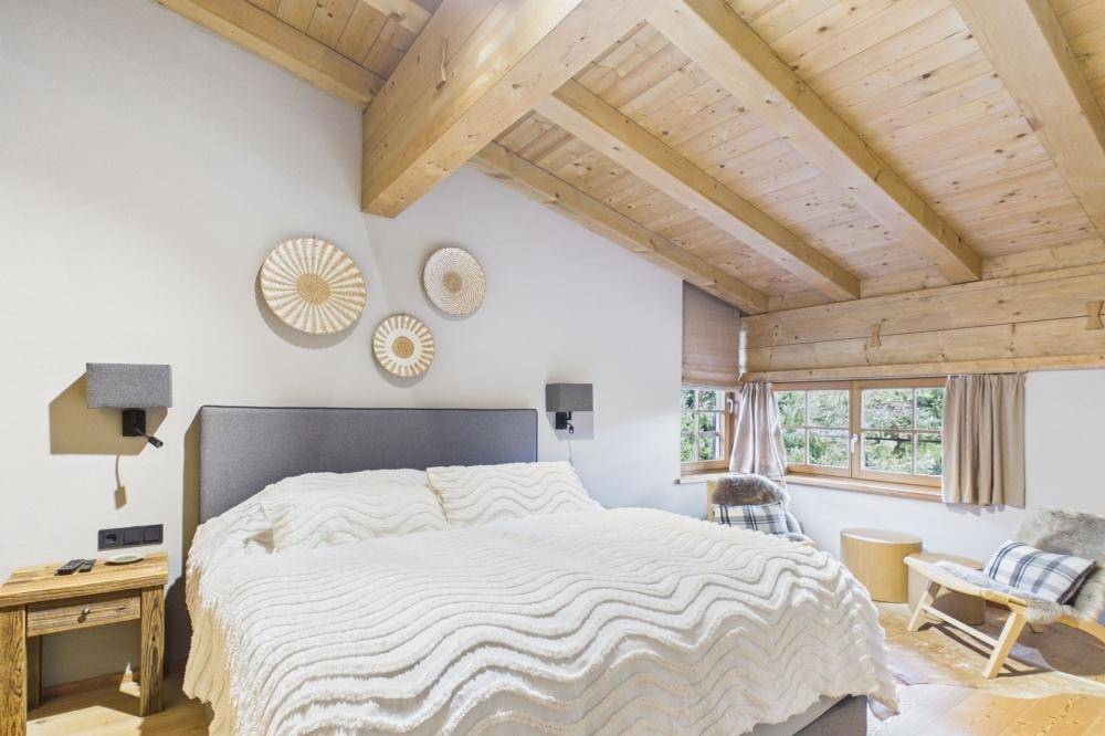 Helles Schlafzimmer mit Holzbalkendecke, Holzboden und Blick ins Grüne.
