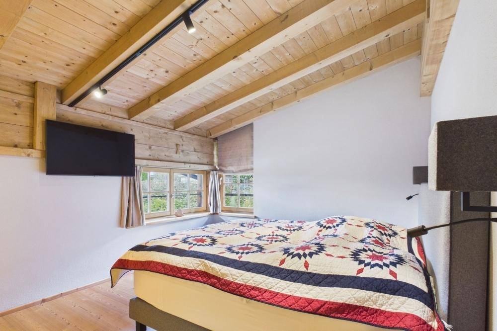 Gemütliches Schlafzimmer mit Holzbalkendecke, Holzboden und Wandfernseher.