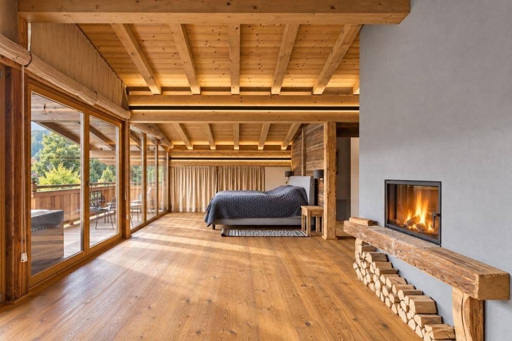Großzügiges Schlafzimmer mit Kamin, Holzbalkendecke und Zugang zum Balkon.