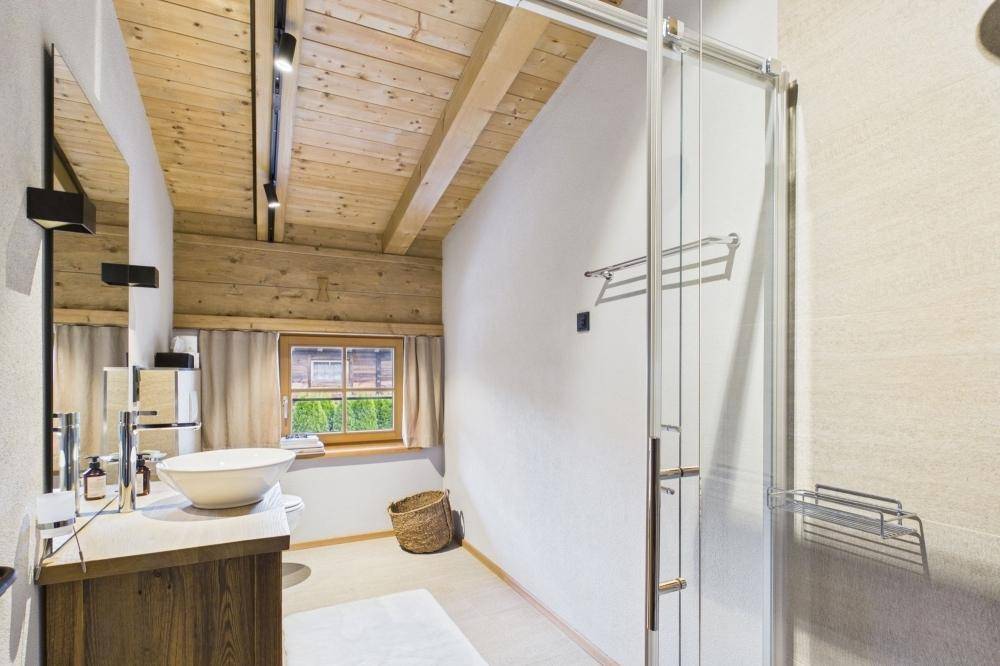 Helles Badezimmer mit Dusche, Holzwaschtisch und Holzbalkendecke.