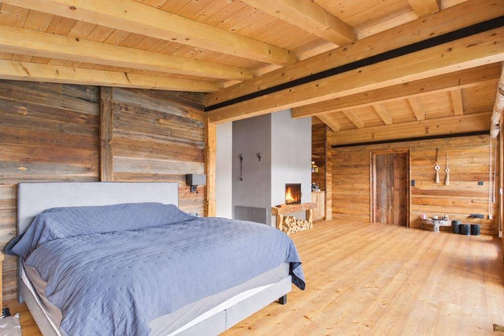 Geräumiges Schlafzimmer mit Holzbalkendecke, Kamin und rustikalen Holzwänden.