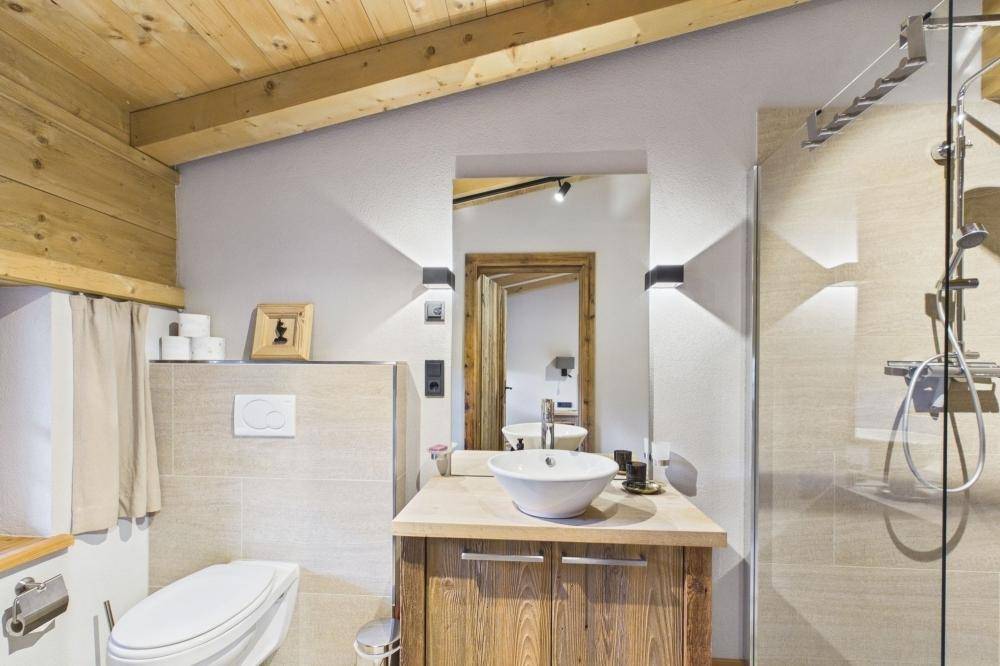 Modernes Badezimmer mit Dusche, WC, Holzwaschtisch und hellen Fliesen.