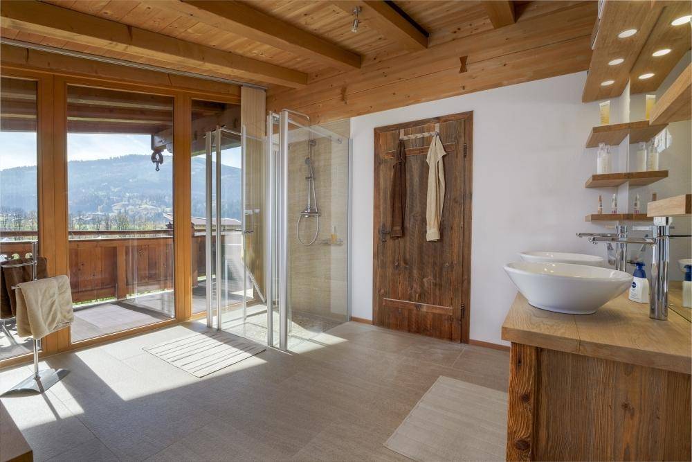 Großes Badezimmer mit Dusche, Doppelwaschbecken und Zugang zum Balkon mit Bergblick.