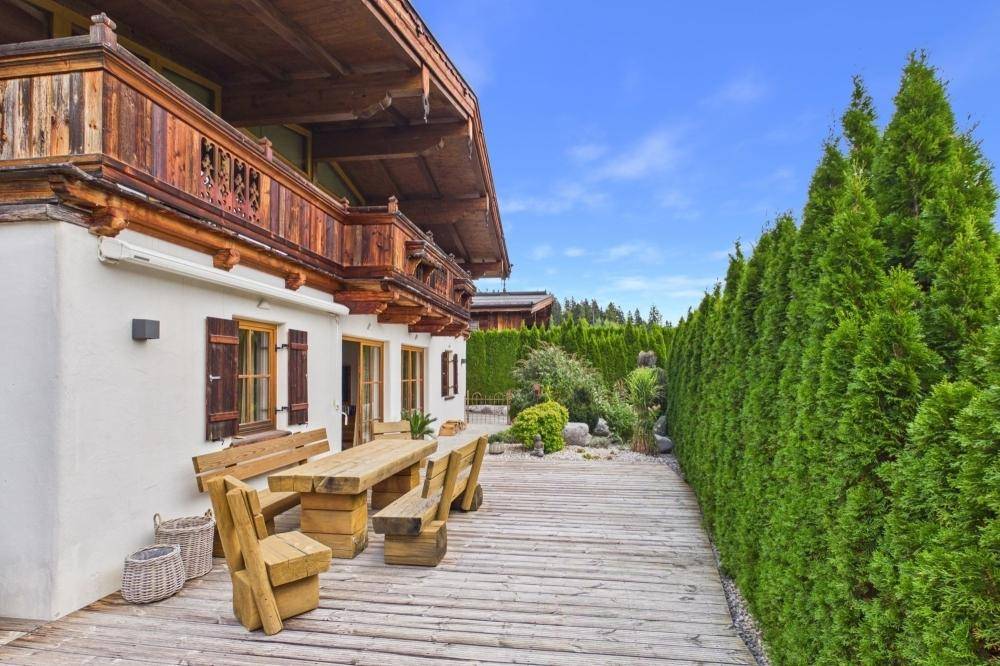 Große Holzterrasse mit Gartenmöbeln und Hecke, ideal zum Entspannen im Freien.