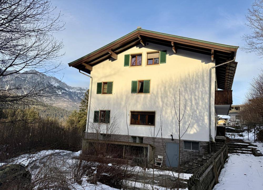 Seitenansicht des traditionellen Hauses mit grünen Fensterläden und Bergblick im Winter.
