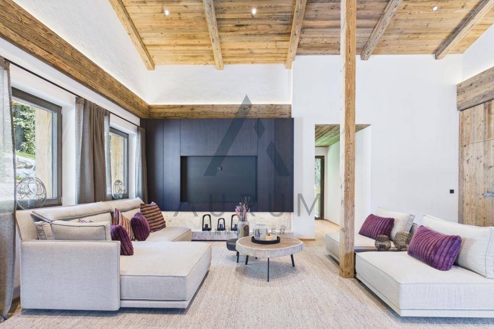 Helles Wohnzimmer mit bequemen Sofas, Holzbalkendecke und integriertem TV-Möbel in dunklem Holz.