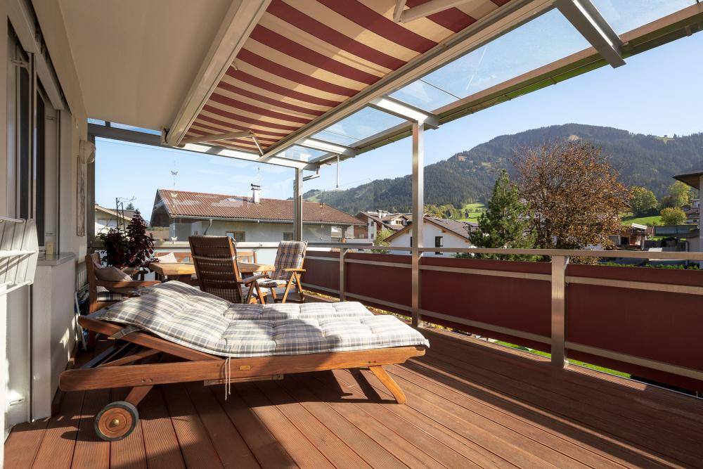 Sonniger Balkon mit Holzdeck, Markise und bequemen Liegestühlen mit Blick auf die Umgebung.