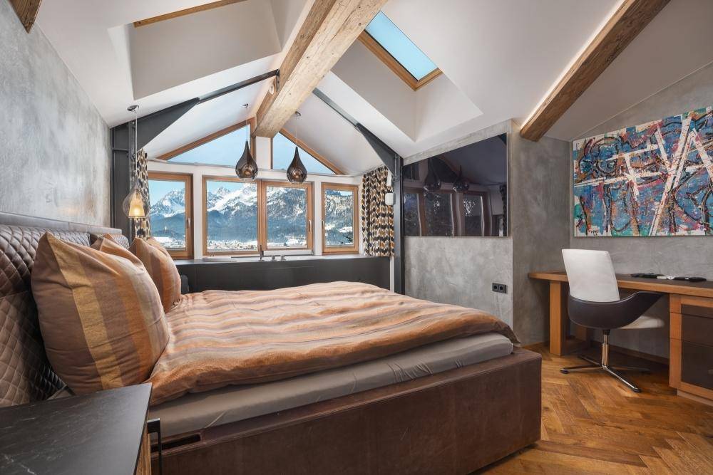 Schlafzimmer im Dachgeschoss mit Holzbalken, Dachfenster und atemberaubendem Bergblick.