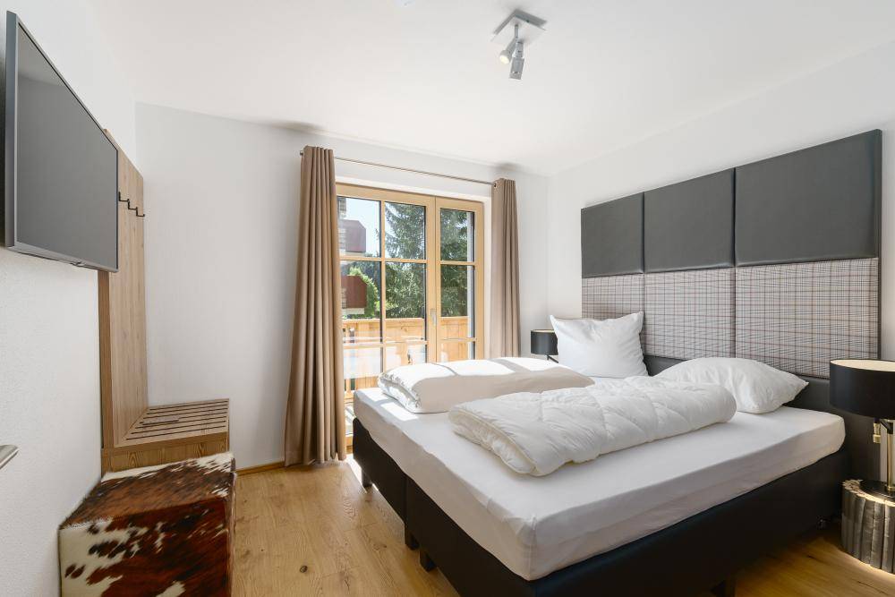 Helles Schlafzimmer mit Doppelbett, Holzboden und direktem Zugang zu einem Balkon.