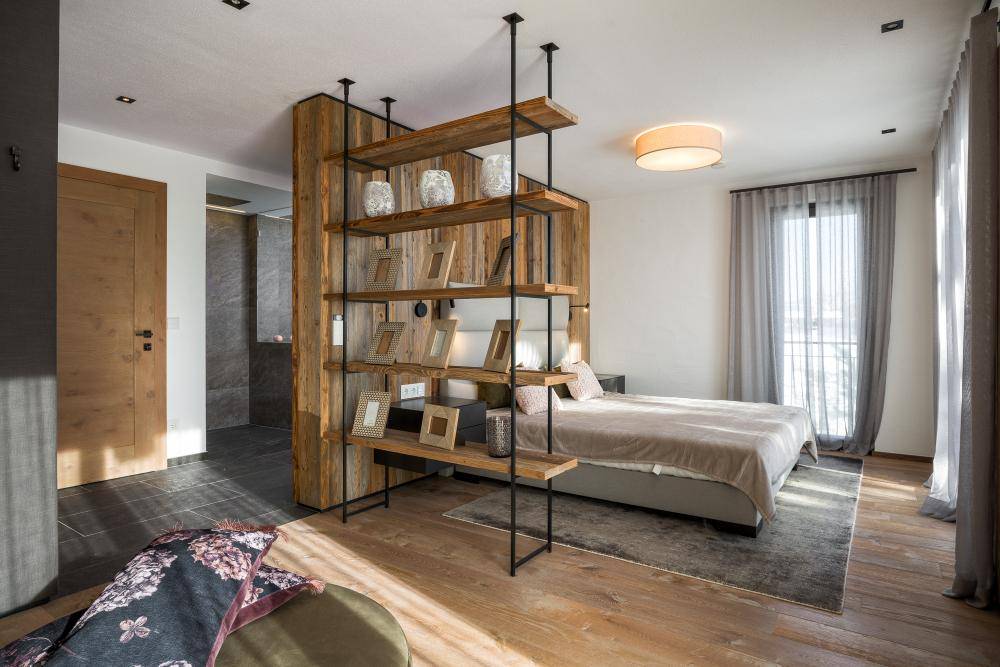 Helles Schlafzimmer mit Holzboden, modernem Bett und offenem Regal als Raumteiler.