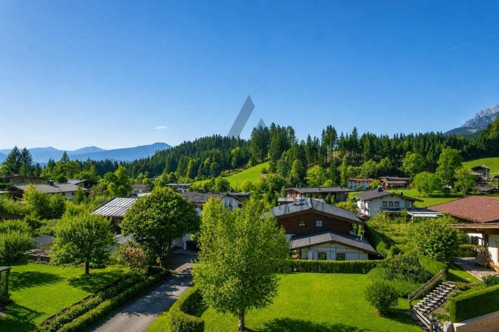 Breiter Ausblick auf eine idyllische Wohngegend mit viel Grün und einer beeindruckenden Bergkette.
