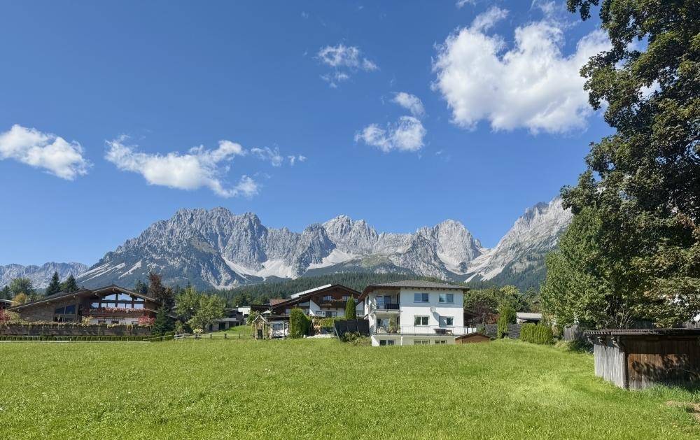 Malerischer Blick auf grüne Wiesen, Häuser und die imposante Bergkette im Hintergrund.
