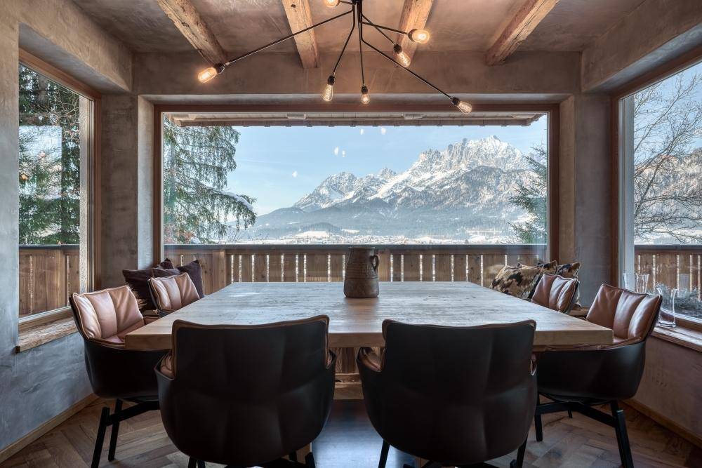 Geräumiger Essbereich mit Holztisch, bequemen Stühlen und beeindruckendem Bergblick durch große Fenster.