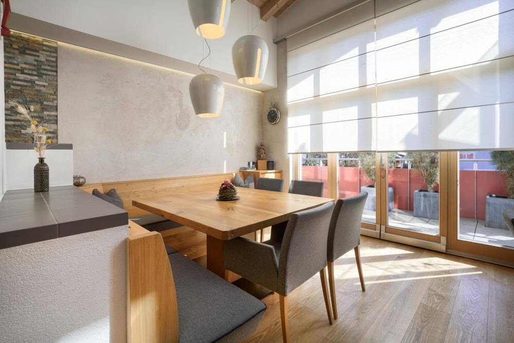 Moderner Essbereich mit Holztisch, Sitzbank und großen Fenstern mit Zugang zur Terrasse.