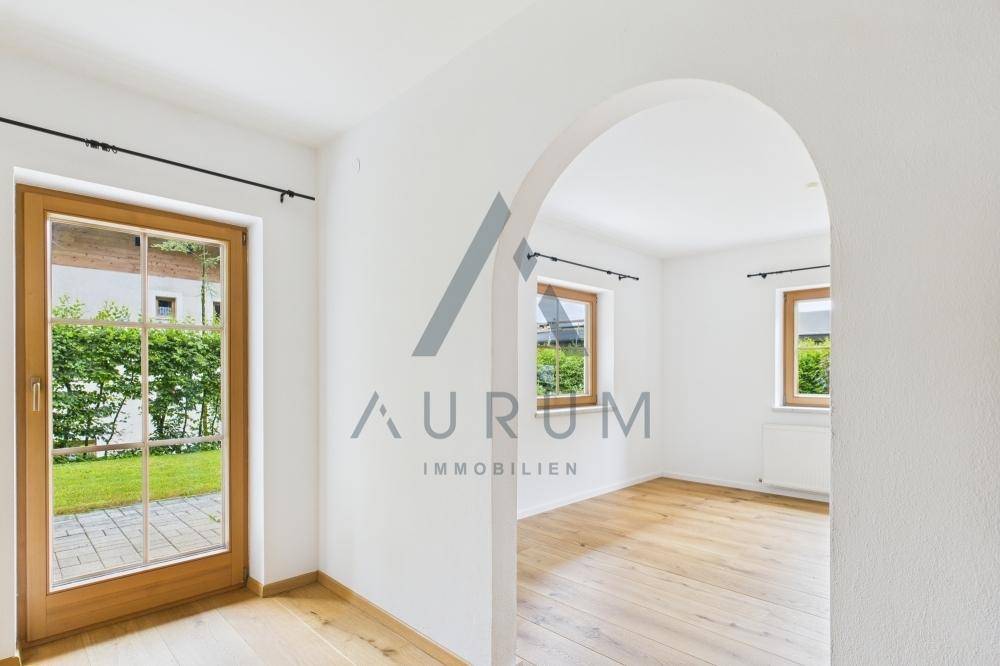 Heller Wohnraum mit Holzboden, einem Rundbogen und direktem Zugang zum grünen Garten.