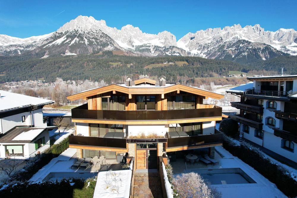 Modernes Mehrfamilienhaus in alpiner Umgebung mit mehreren Balkonen und Terrassen im Winter.