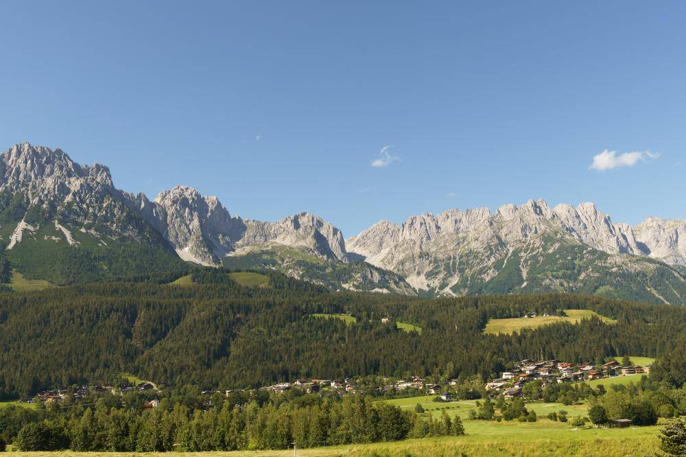 Weitläufiger Panoramablick auf die beeindruckende Bergkette und ein idyllisches Tal mit Siedlung.